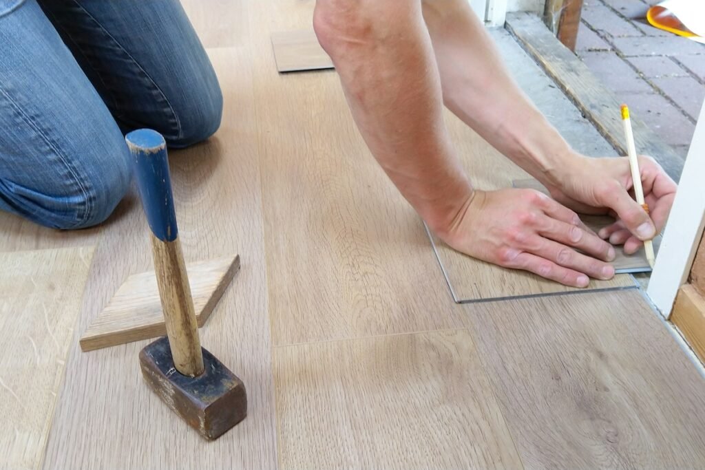 A man is working on a wooden floor with a hammer, providing Residential Flooring Solutions.